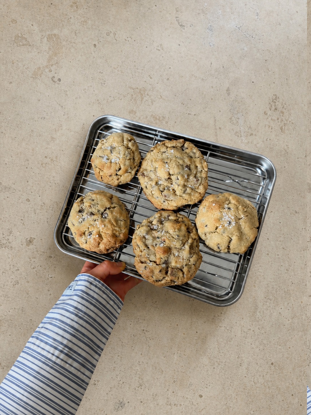 Five New York chocolate chip cookies on a tray held by a striped sleeve