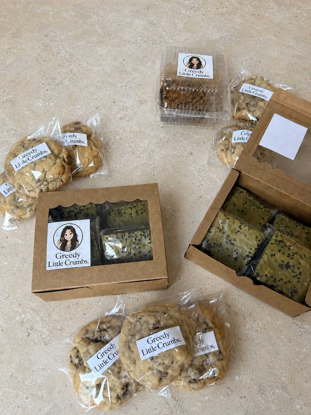 Greedy Little Crumbs boxes and individually wrapped bakes arranged on a stone worktop